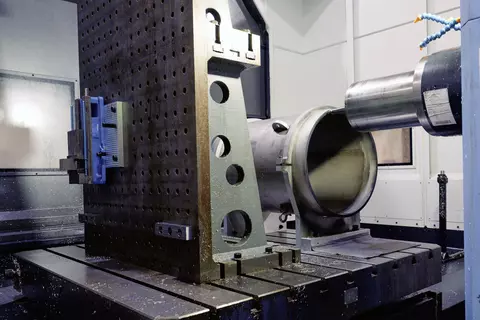 A cylinder of thick metal lies horizontally on a large support structure inside a workshop.