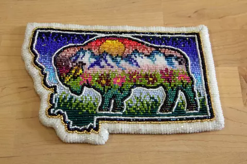 A beaded patch in the shape of Montana features a buffalo with a colorful mountain scene inside. 