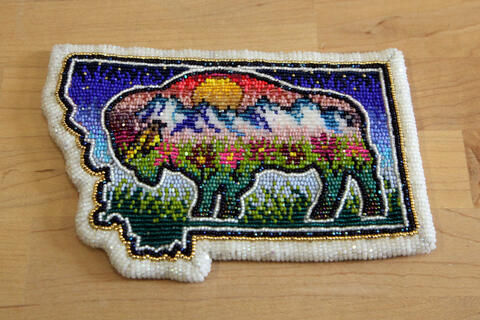 A beaded patch in the shape of Montana features a buffalo with a colorful mountain scene inside. 