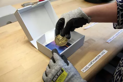 A gloved hand holds a commemorative coin featuring Theodore Roosevelt over an open white box. 