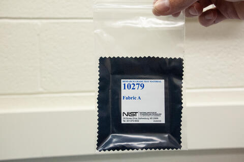 Hand holding plastic bag with blue square of fabric material labeled 