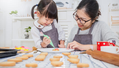 Young girl icing a cookie with family member.