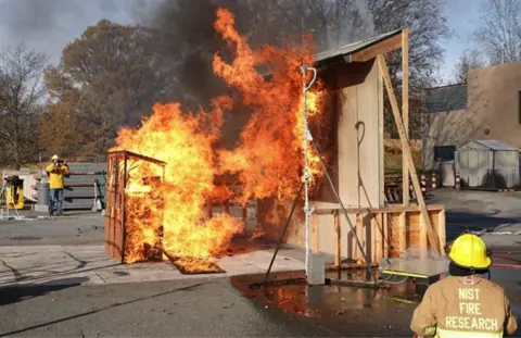 A very small wooden shed filled with 6 wood cribs, separated by 3.2 m (10 ft) from the target, and burning under a high wind condition creates a large plume of flame that contacts the target wall.