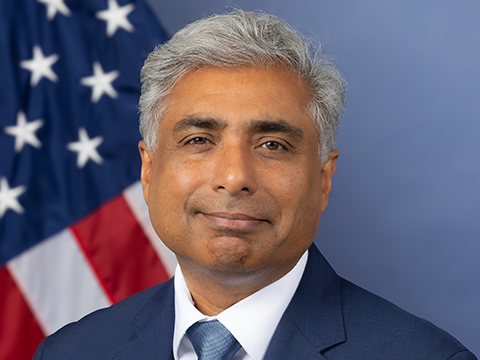Arvind Raman poses for an official U.S. headshot with the American flag behind him.