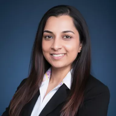 Professional headshot of Simona Patange, a woman with long dark hair, smiling, wearing a white collared shirt and black blazer. smiling