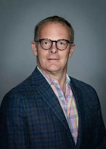 Professional headshot of Christopher Soles, a man with short brown hair, wearing glasses, a collared shirt, and a suit jacket.