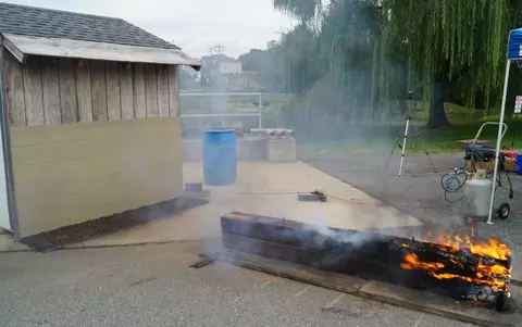 A photo of a stack of two railroad ties burning in front of a shed. The ties are 2.59 meters or 8.5 feet long and are 36 cm or 14 inches tall at a distance of 1.83 meters or 6 feet from the shed. The ties are oriented perpendicular to the face of the shed.