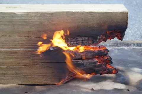 A photo of a close-up view of burning landscape timbers. The timbers are a stack of two six-by-six dimensional treated pine lumber. Fire is progressing mostly between and under the two timbers.