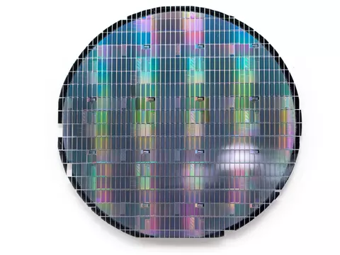 Circular sheet holds hundreds of tiny metallic rectangles reflecting rainbow colors. 