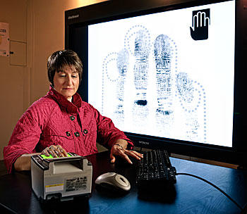 Woman with her hand on a fingerprint scanner with a screen in the background showing her fingerprint scans