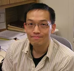 Headshot of Vincent Shen, a man with short black hair and glasses, wearing a collared button up shirt, sitting at a desk.