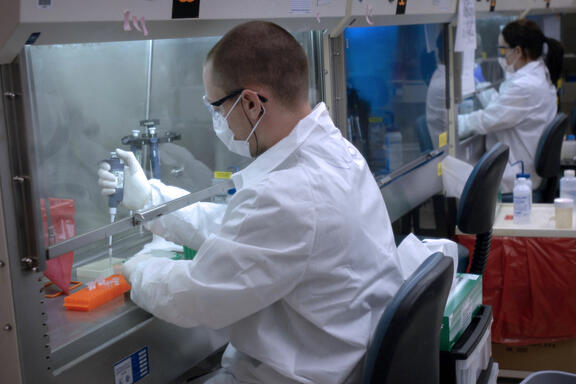 Man in white lab coat using a pipette under a hood