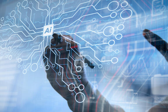 Hands draw on a transparent screen with circuits making the shape of a brain and "AI" written in the center. 
