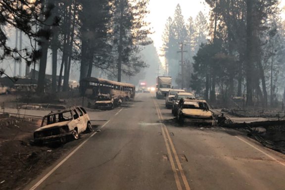 A two-lane highway lined with the burnt remains of vehicles that were destroyed by fire while in traffic..