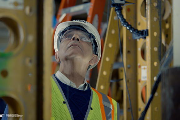 Photo of structural elements surrounding man with helmet and glasses looking up 