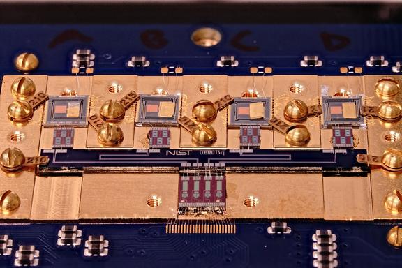 Circuit board with various square chips and gold screws. Small letters in the center say: NIST True Bq.