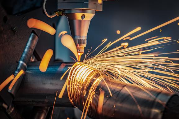 Sparks shoot off as a laser cutting head slices a metal pipe into thin circles.