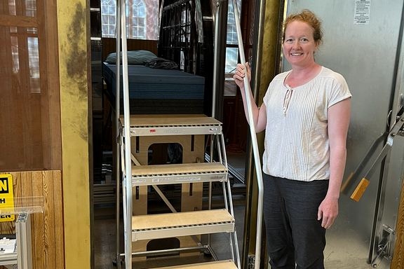 Woman poses smiling next to a set of portable stairs that lead up to a platform for an experimental MRI setup. 