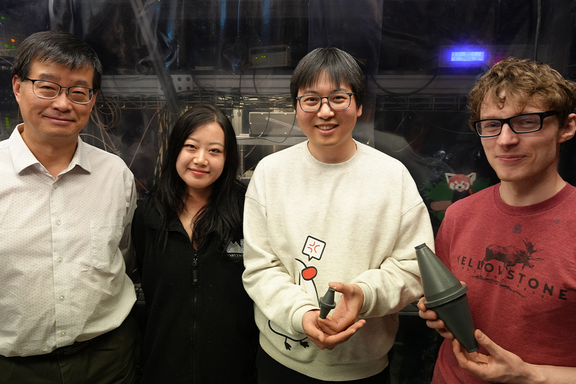 Four researchers, one older and three younger, pose in the lab holding models of a laser cavity.