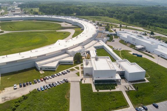 An arial view shows part of the huge enclosed loop of an accelerator, with attached buildings and parking lots.