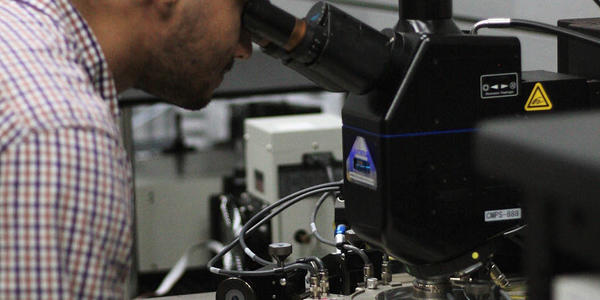 Samuel Márquez Gonzalez leans forward to look through a microscope in the lab. 