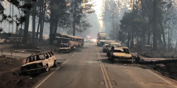 A two-lane highway lined with the burnt remains of vehicles that were destroyed by fire while in traffic..