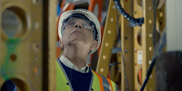Photo of structural elements surrounding man with helmet and glasses looking up 