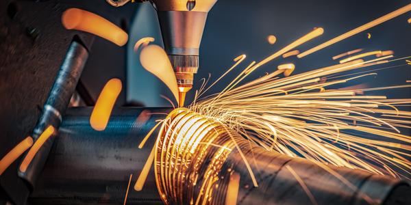 Sparks shoot off as a laser cutting head slices a metal pipe into thin circles.
