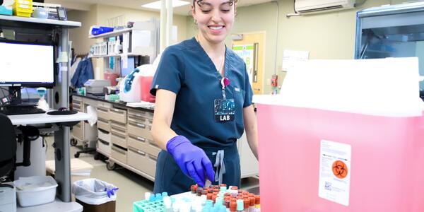 A medical worker in scrubs places a vial into a rack in a medical lab. 