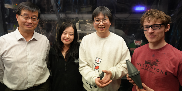 Four researchers, one older and three younger, pose in the lab holding models of a laser cavity.