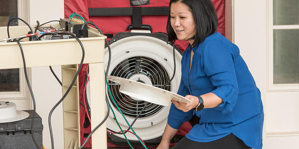 Lisa Ng kneels, holding parts of a circular fan built into a room divider. 
