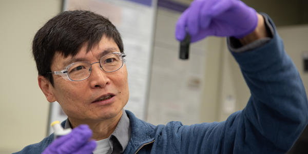 Researcher Ming Zheng looks with interest at a small vial he is holding up in front of him. 