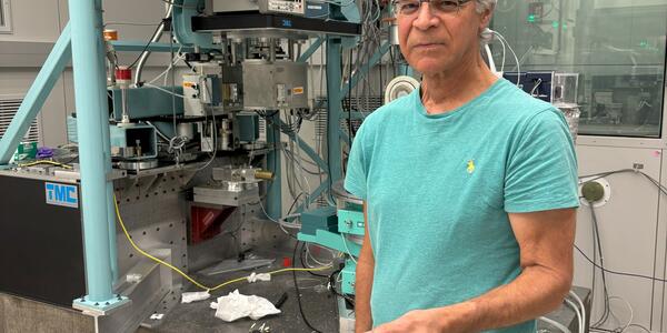 Jim Cline stands in front of a large scientific device in a lab, holding a small white disk.