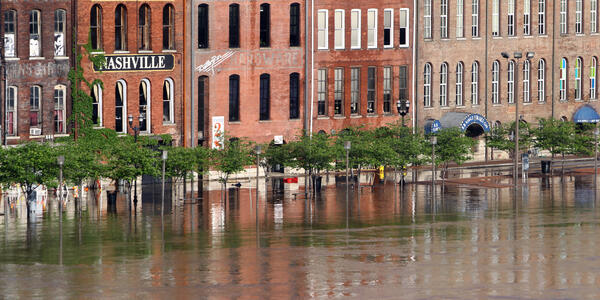 Floodwaters rise to the doorways of a row of historic brick buildings, one with a sign saying "Nashville."