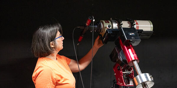 Susana Deustua looks at a large, red telescope located in a dark room. 