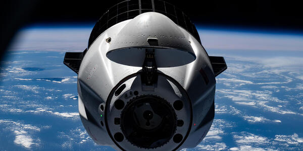 A rounded spacecraft floats in space with the blue surface of the Earth in the background.