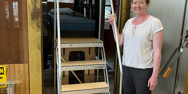 Woman poses smiling next to a set of portable stairs that lead up to a platform for an experimental MRI setup. 