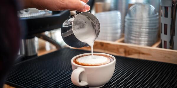 A barista pours steamed milk into a cup of espresso.