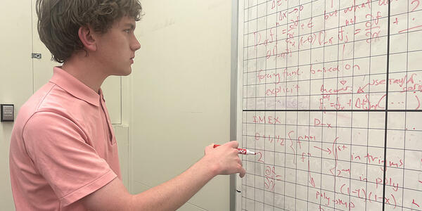Henry Nonnemaker stands holding a marker, looking at a gridded whiteboard covered with mathematical formulas.