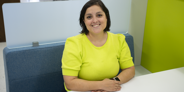 NIST researcher Carina Hahn, wearing a lime green sweater, sits at a white table and smiles at the camera. 