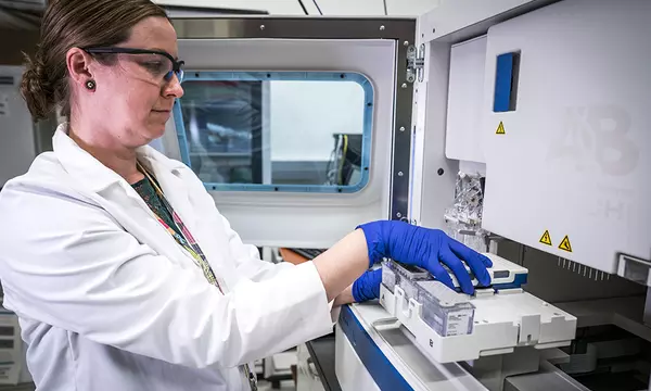 woman loads small plastic vials containing human DNA into a large machine