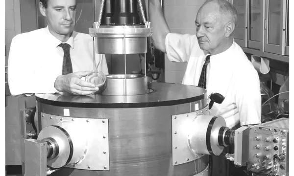 Two men stand on either side of a large cylindrical device.