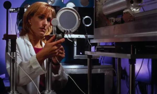 A woman in a lab coat adjusts a piece of scientific equipment