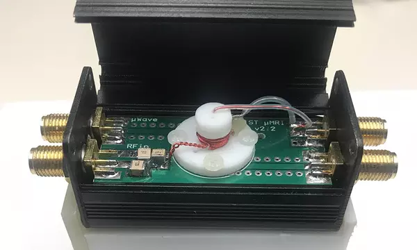 a small box with cable pairs of cable outlets coming out of either end. the box top is open and there is circuitry and a white nipple shaped piece in the center.