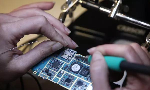 A closeup photograph of person's hands as they solder a wire onto a circuit board.