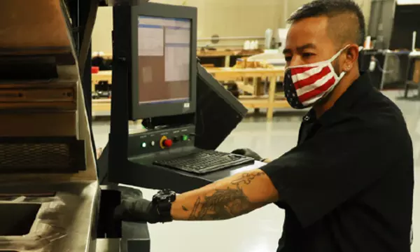 manufacturing worker in a US flag mask operating equipment