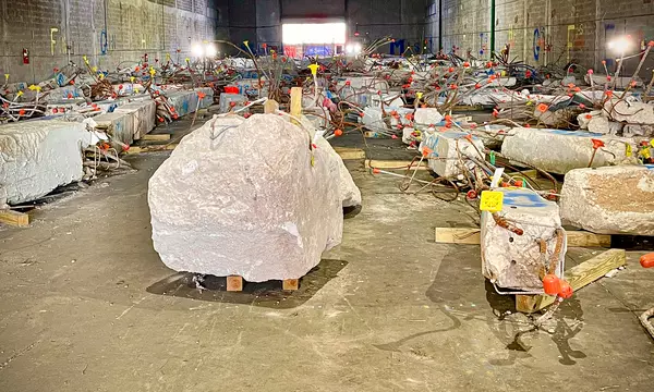 Large chunks of concrete bristling with rebar and colored flags sit in a warehouse. 