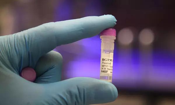 A gloved hand is holding up a small plastic vial labeled "RGTM plasmid."