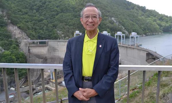 Jeffrey Fong poses smiling in front of a railing overlooking a concrete dam. 