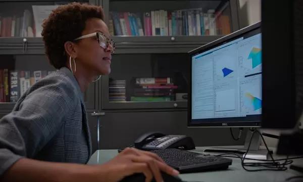 Side view of Danielle Brager at a desk, looking at a monitor, hand on a computer mouse.